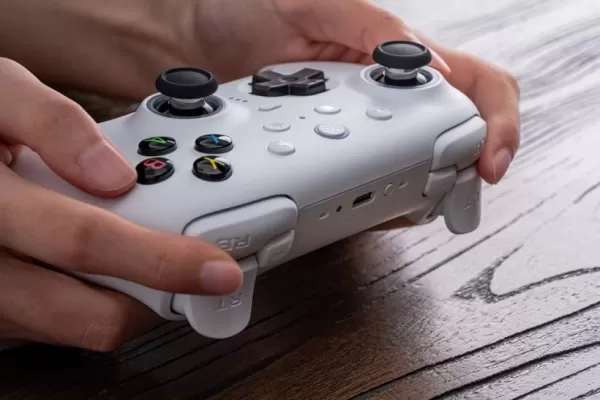 Una imagen de una persona que sostiene un controlador de juego blanco en un escritorio de madera